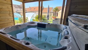 A hot tub with a view of a garden and neighboring houses. - Cottage Atypique (Mosnes)