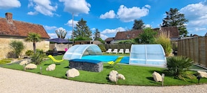 A backyard with a swimming pool, a covered seating area, and a greenhouse structure.