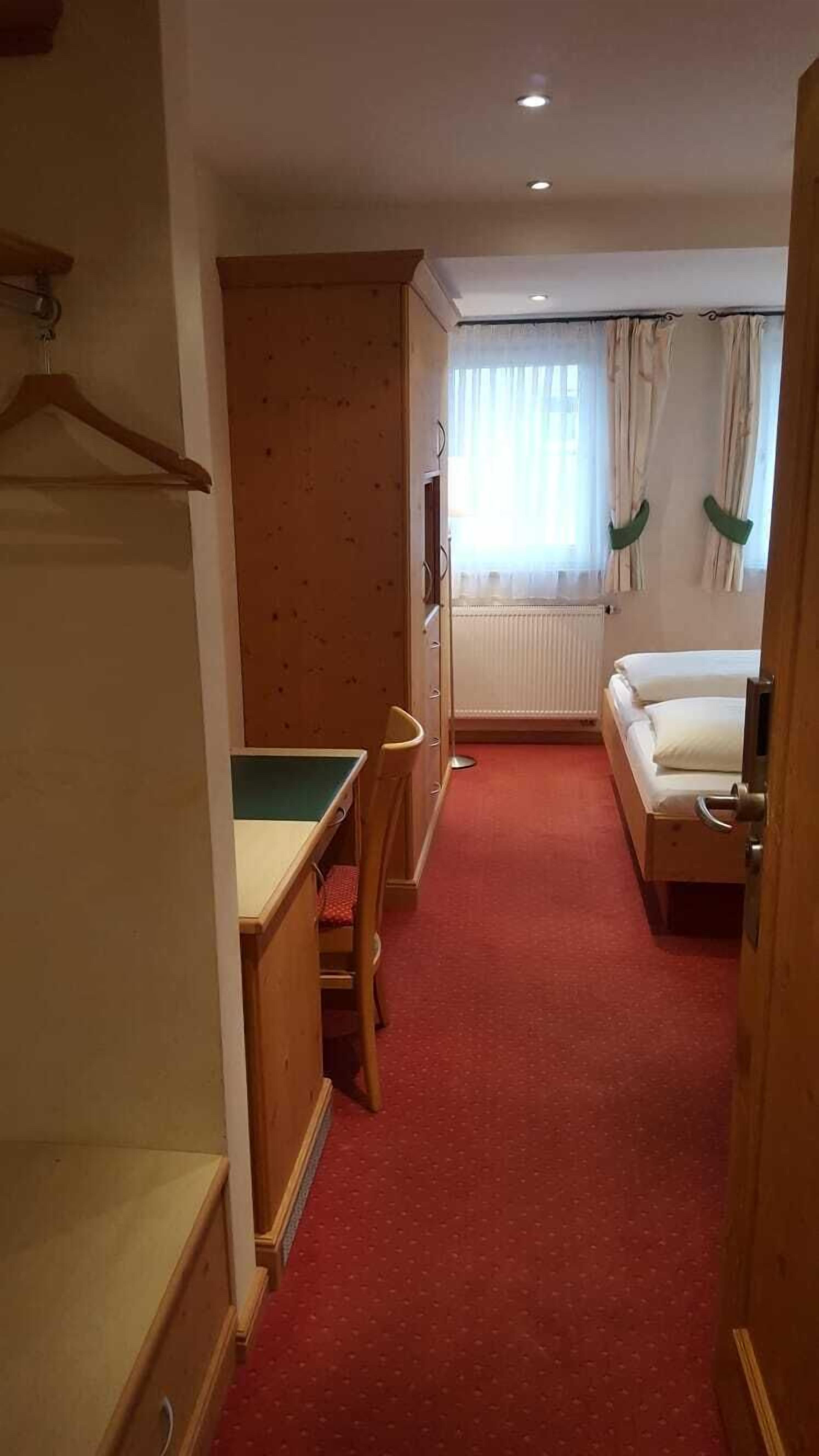 A narrow hallway with a bed, a desk, and a radiator.