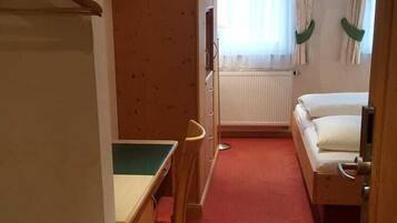 A narrow hallway with a bed, a desk, and a radiator.