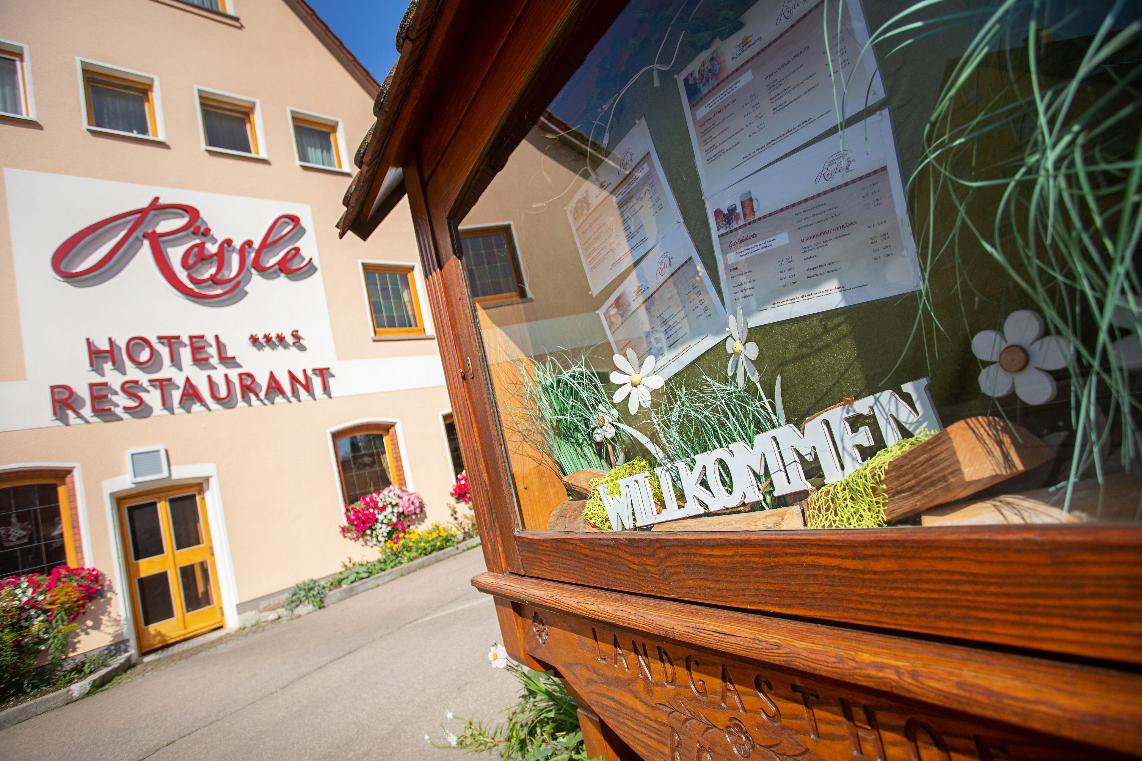 Un cartel de hotel con 'Rössle Hotel Restaurant' y un cartel de bienvenida con 'Willkommen' en primer plano.