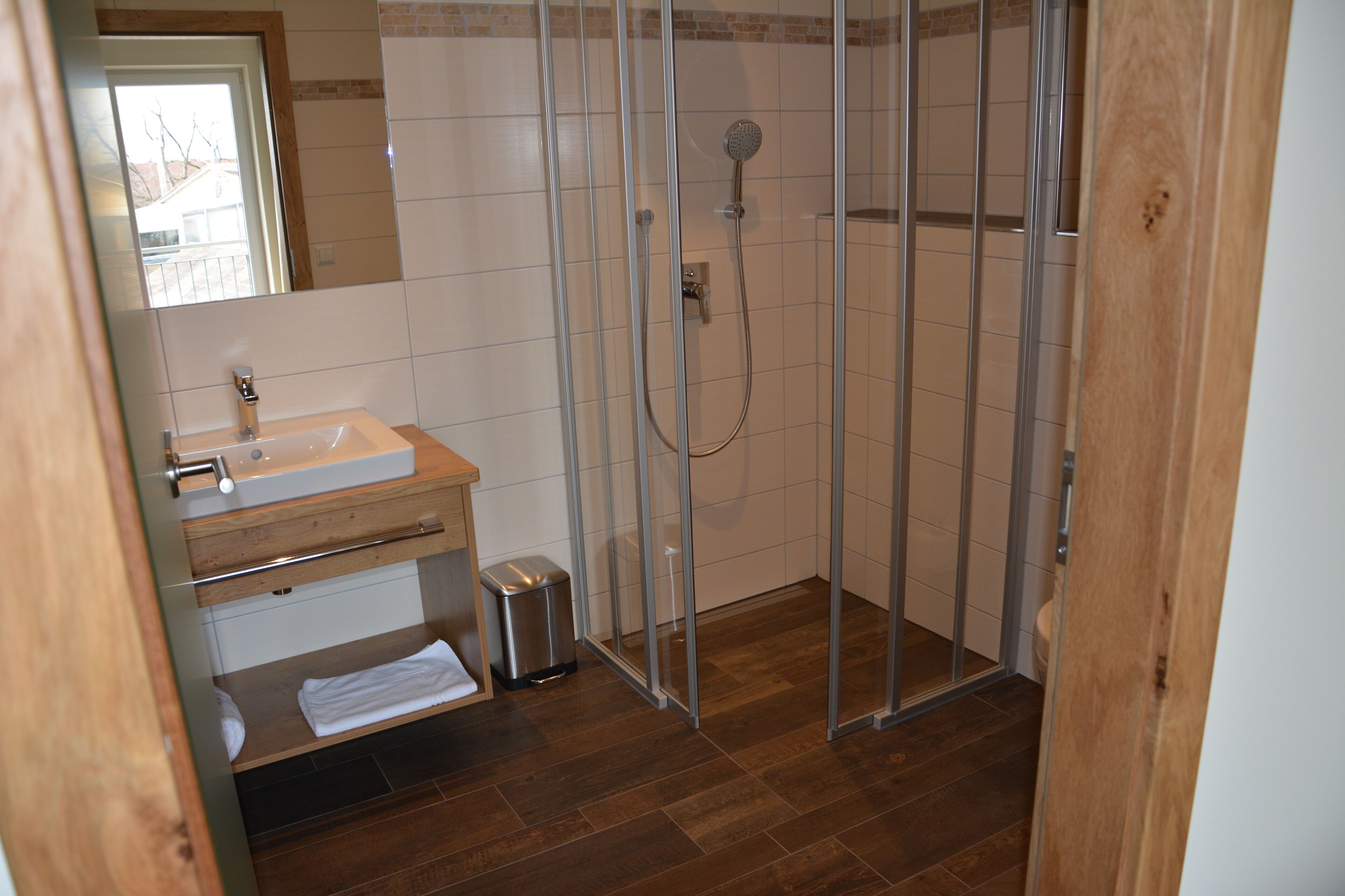 A bathroom with a wooden vanity, a glass shower enclosure, and a tiled floor.