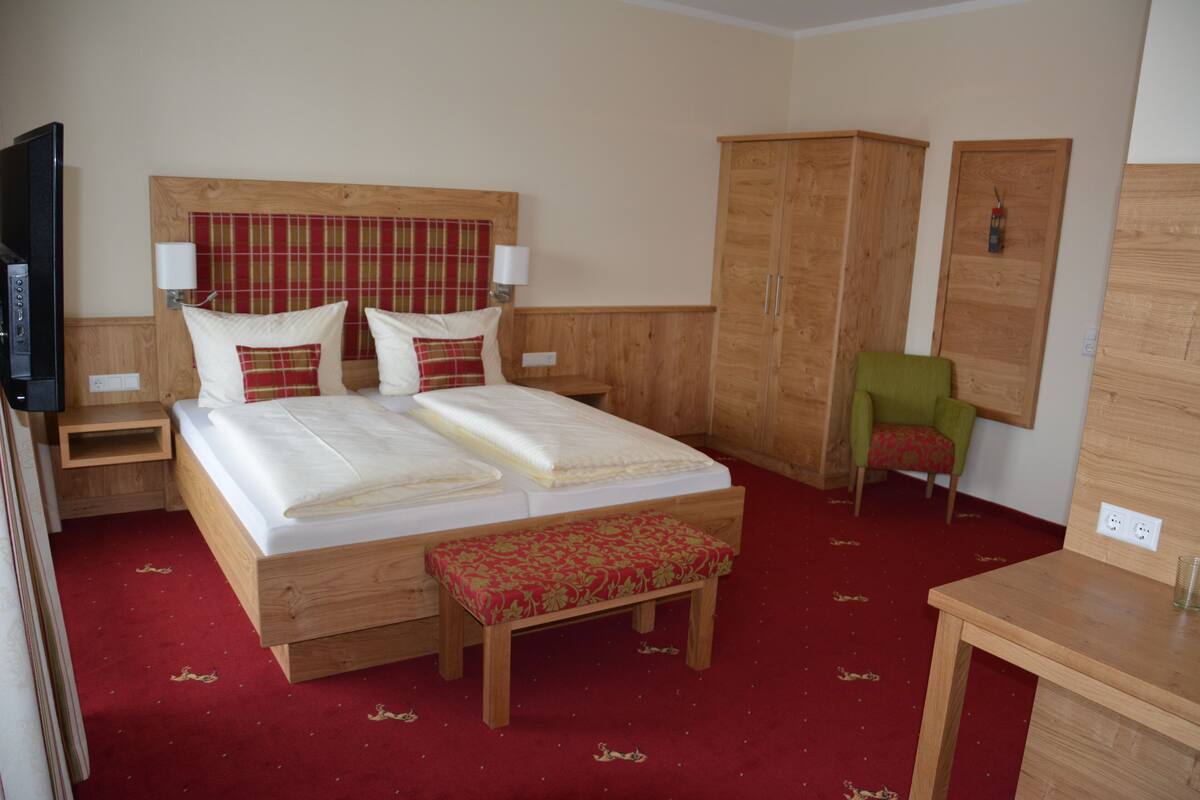 Ein Hotelzimmer mit einem hölzernen Bett, einer Bank, einem grünen Sessel und einem Holzschrank.