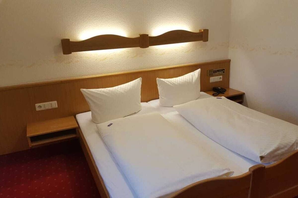 Ein Doppelbett mit weißer Bettwäsche, ein hölzerner Kopfteil, Nachttische und eine an der Wand befestigte Leuchte.