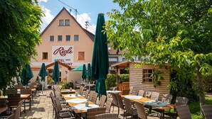 An outdoor patio area with wicker furniture and green umbrellas, a building with a sign reading "Resale Hotel", and a wooden structure to the right. - Landgasthof Hotel Rössle (Boehmenkirch)