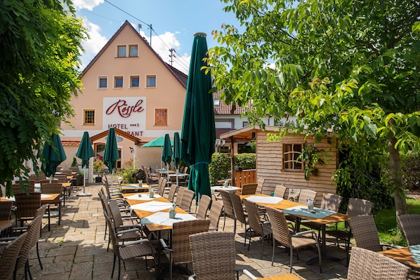An outdoor patio area with wicker furniture and green umbrellas, a building with a sign reading "Resale Hotel", and a wooden structure to the right.