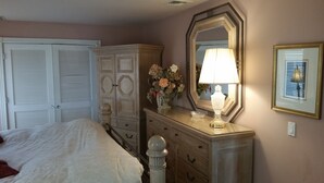 A bedroom with a bed, a dresser with drawers, a mirror, a vase with flowers, and a lamp. - NEW LISTING! Beachfront Villa (Manasquan)
