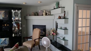 A living room with a fireplace, a chair, a fan, and shelves with decorative items. - NEW LISTING! Beachfront Villa (Manasquan)
