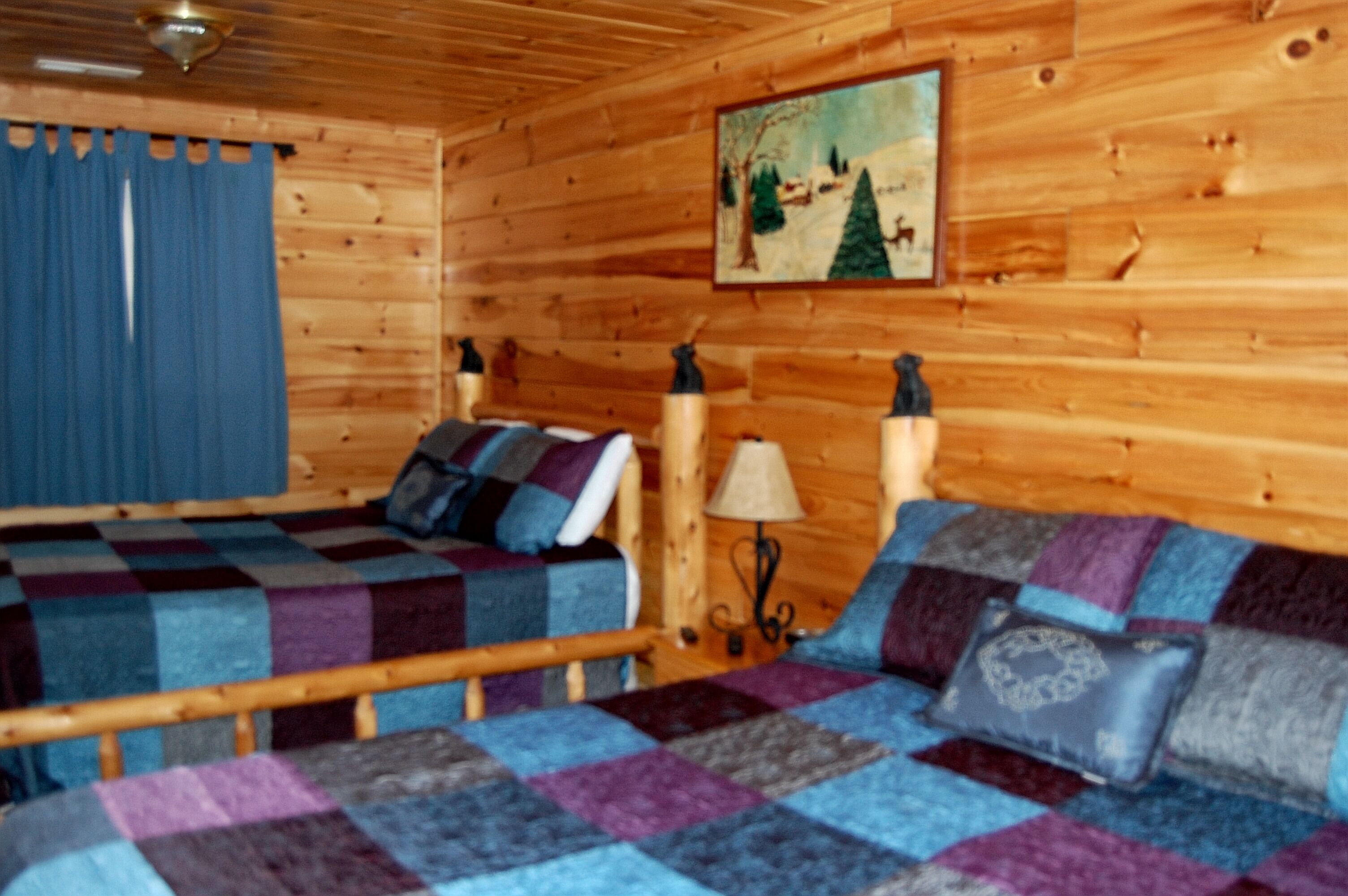 Une pièce de style cabane en bois, avec un lit, une lampe et un tableau accroché au mur.
