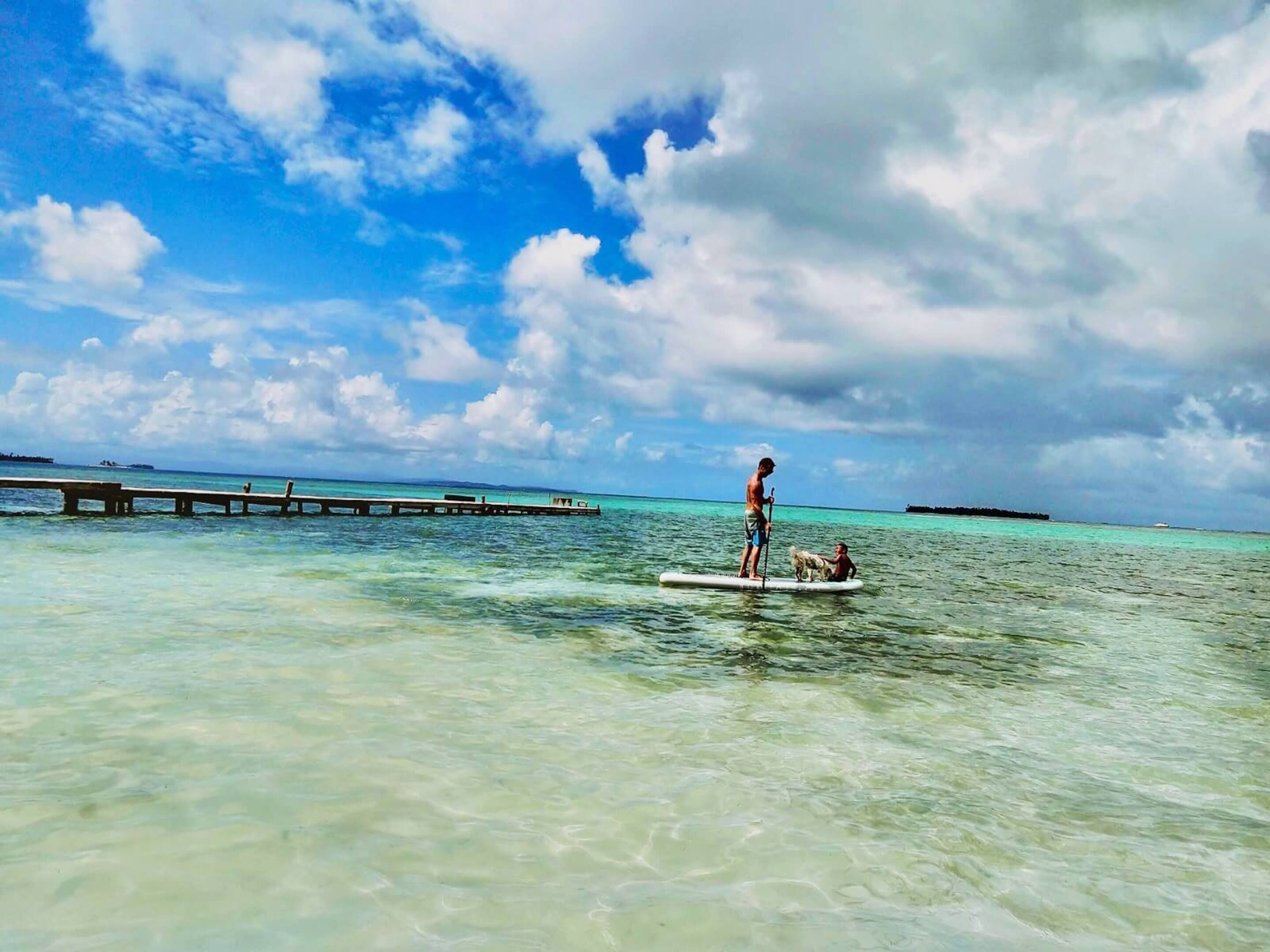 Een heldere turquoise zee met een houten steiger die erin uitloopt.