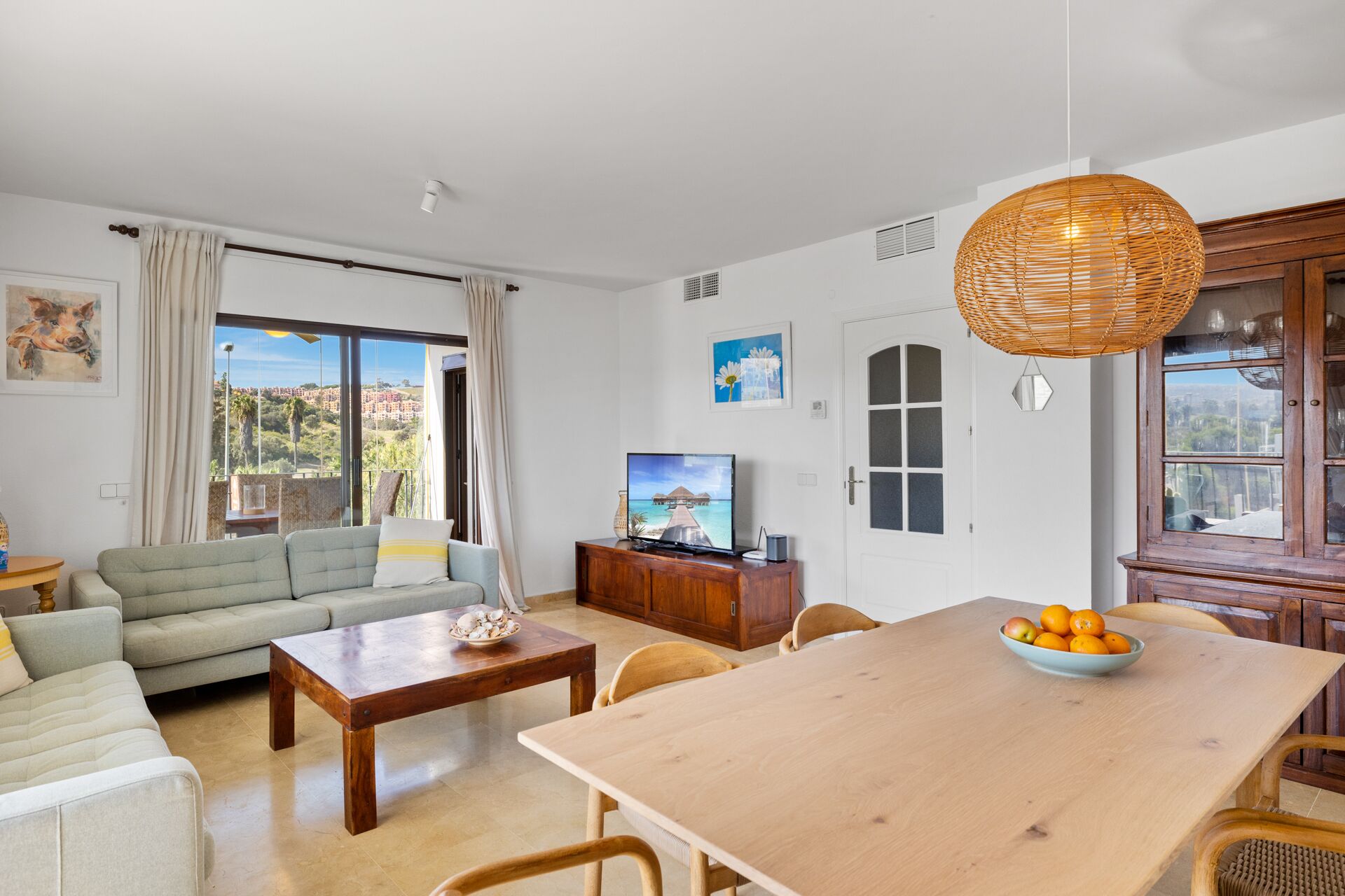 A living room with a sofa, coffee table, TV, dining table with chairs, and a view of the city through large windows.
