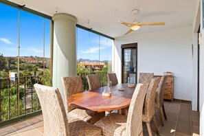 A spacious balcony with a wooden dining table and wicker chairs, offering a view of a residential area and mountains. - Luxurious and bright apartment on the Costa del Sol (Puerto de la Duquesa)