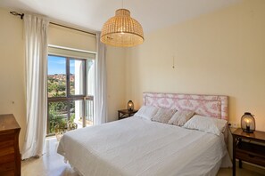 A bedroom with a large bed, a window with curtains, a bedside table with a lamp, and a hanging light fixture. - Luxurious and bright apartment on the Costa del Sol (Puerto de la Duquesa)
