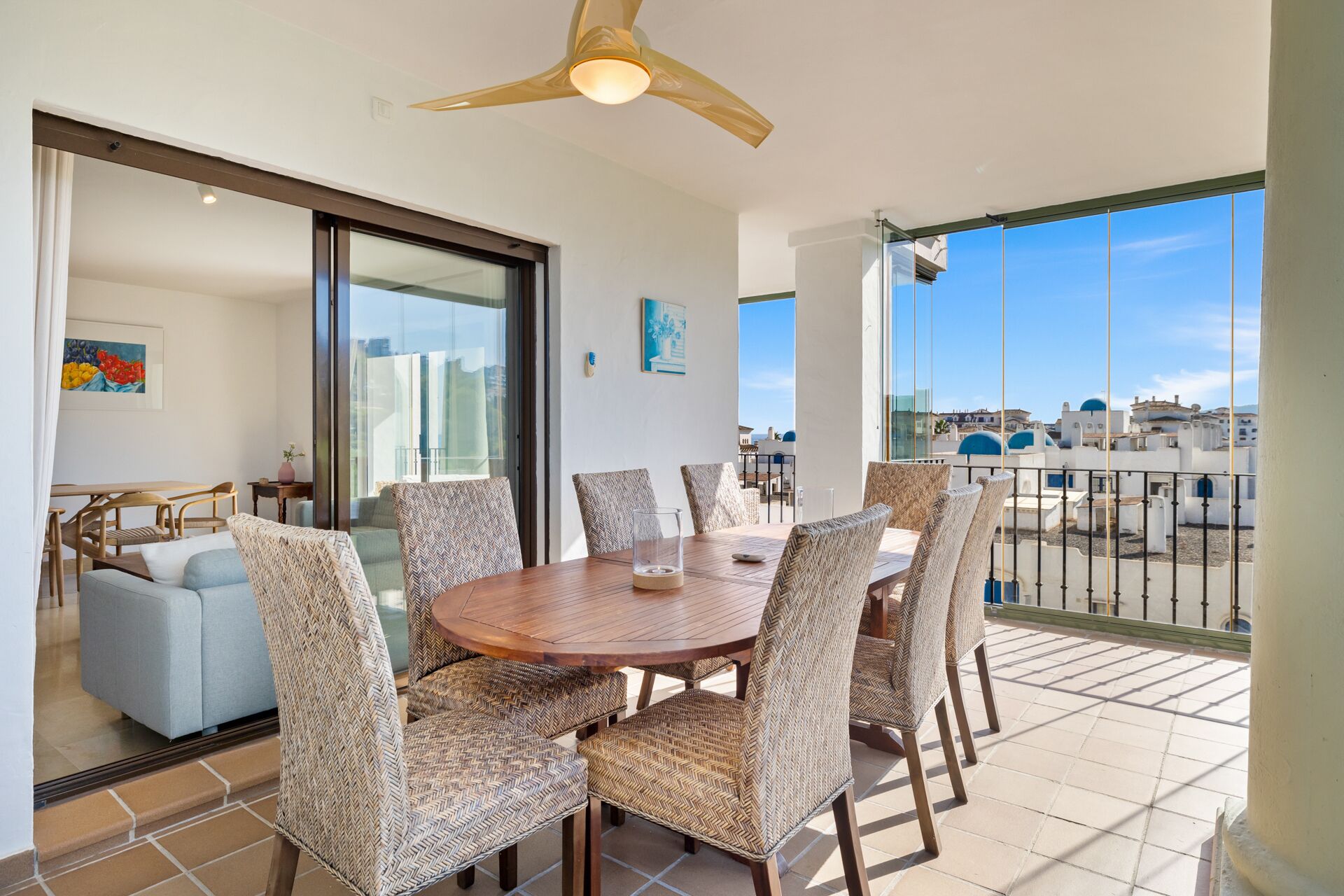 A balcony with a dining table and chairs, a ceiling fan, and a view of buildings with blue domes.