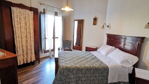 A bedroom with a wooden bed, a nightstand, a chair, a wooden floor, a ceiling fan, and a window with curtains. - Agriturismo Torre Mannella (Citta Sant'Angelo)