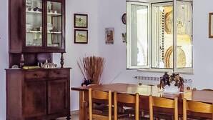 A dining area with a wooden table and chairs, a cabinet with glass doors, and a window with open shutters. - Agriturismo Torre Mannella (Citta Sant'Angelo)