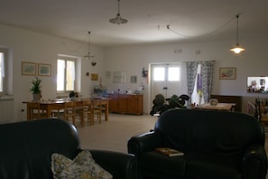 A spacious living room with a dining area, a kitchen in the background, and a large window with curtains. - Agriturismo Torre Mannella (Citta Sant'Angelo)
