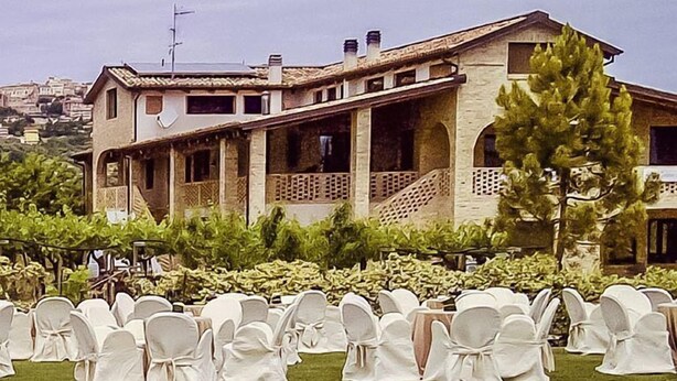 A poolside area with rows of white chairs, a building with a balcony, and a clear sky. - Agriturismo Torre Mannella (Citta Sant'Angelo)