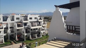 Un edificio moderno con fachada blanca y balcones, con montañas al fondo.