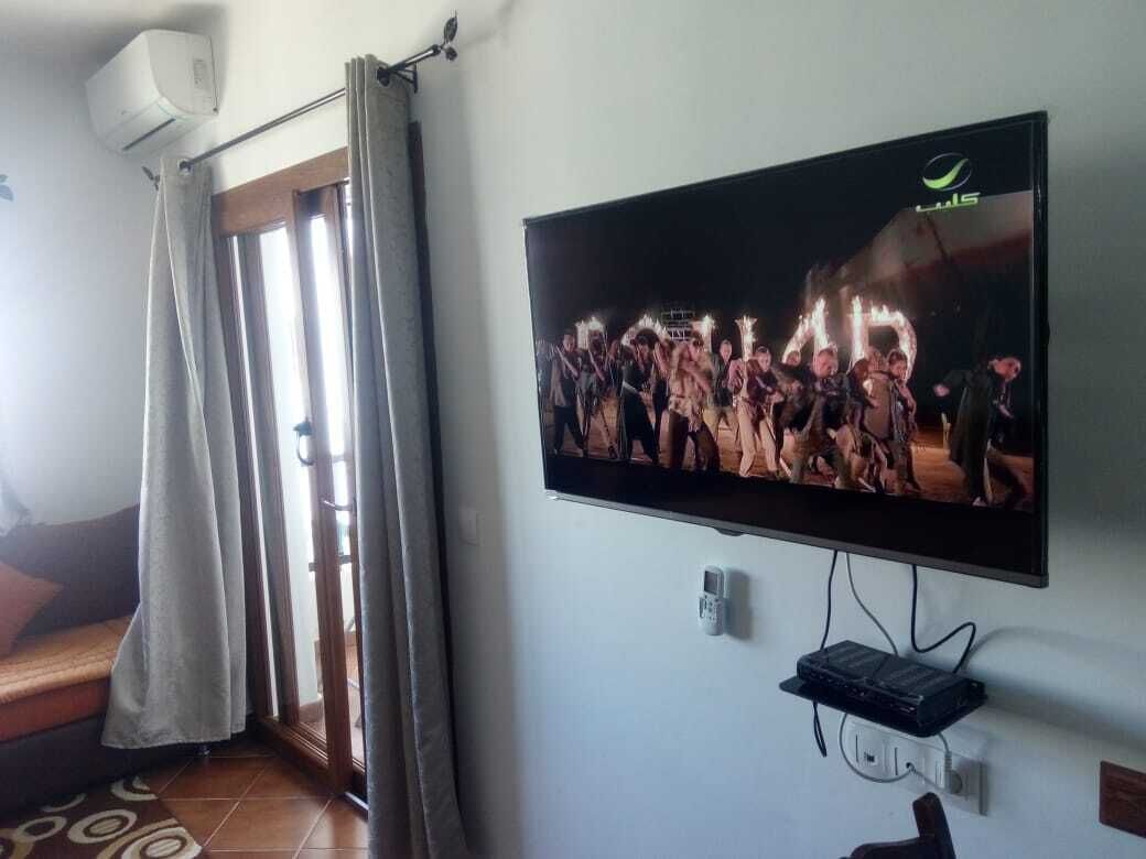 A television mounted on a wall, a power outlet, and a window with curtains.