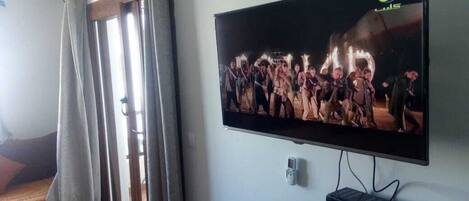 A television mounted on a wall, a power outlet, and a window with curtains.