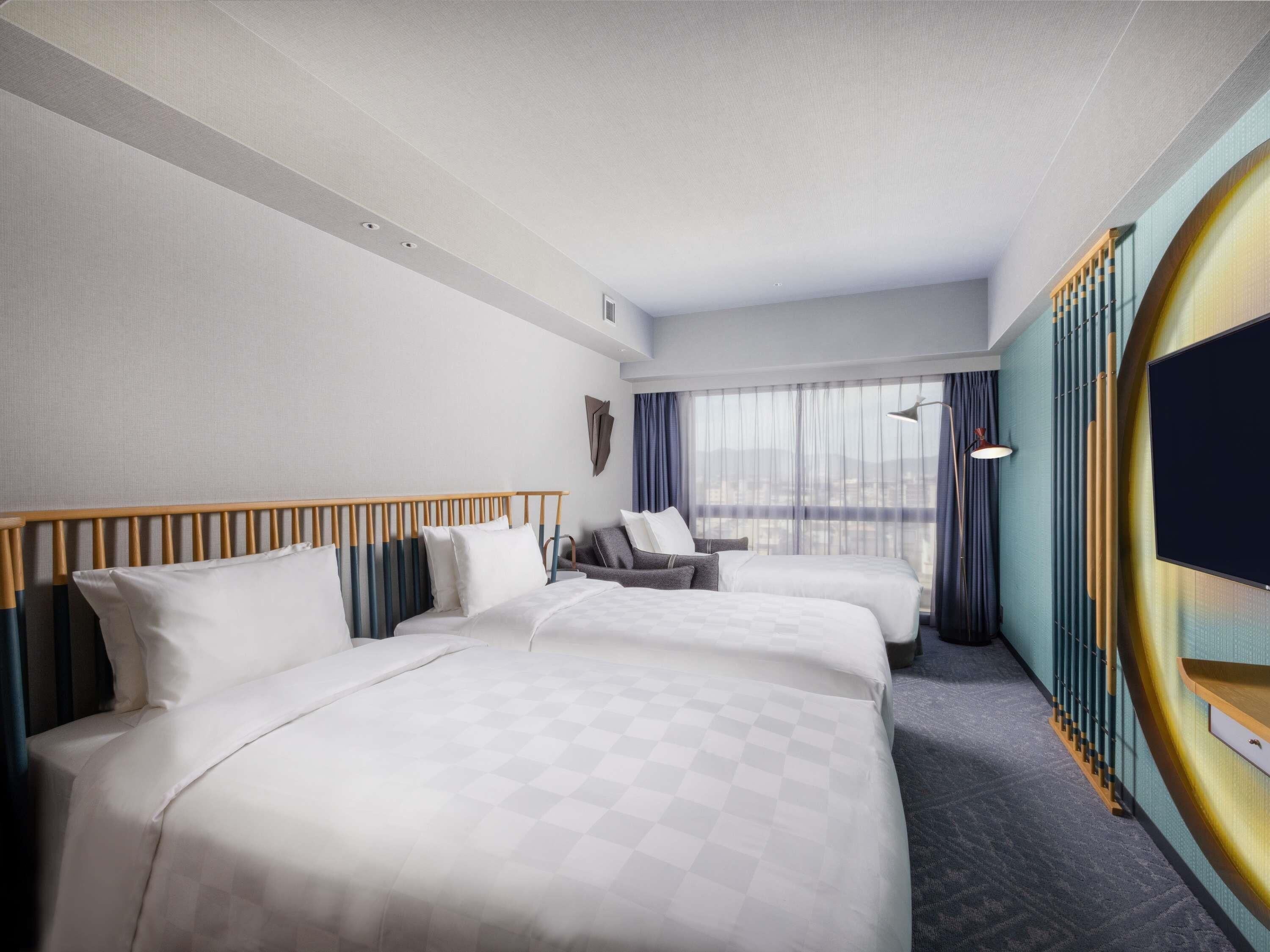 Une chambre d’hôtel avec deux lits, un canapé, une télévision et une vue sur la ville.