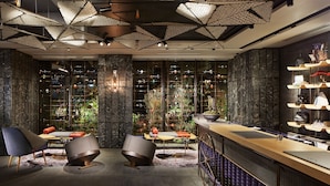 Un bar moderno con una barra larga, asientos con mesas redondas y vistas de la ciudad a través de amplios ventanales.