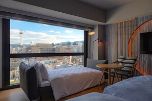 Moderni hotellihuone, jossa on suuri ikkuna, sänky, pieni pöytä, tuoli ja seinälle asennettu televisio.