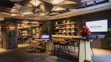 A bar area with a digital screen, seating, and a display of Mercure Hotels.
