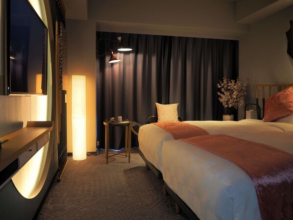 Habitación de hotel con cama, una mesita, lámpara, televisión y ventana con cortinas.