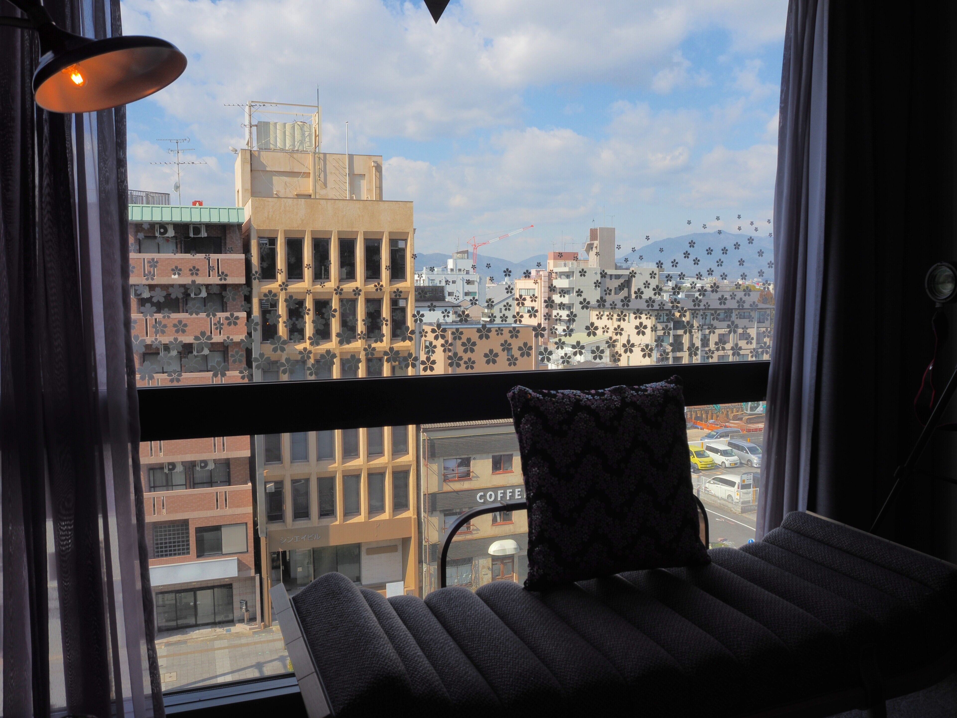 Un balcón con una silla y un cojín, con vistas a un paisaje urbano con edificios y una cafetería.