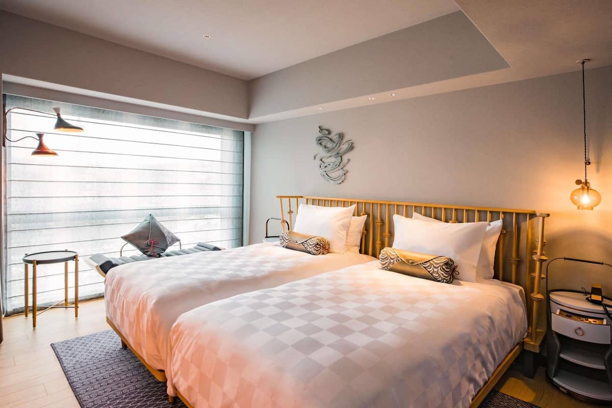 Una cama doble con un edredón de cuadros, una mesita de noche con una lámpara y una ventana con persianas.