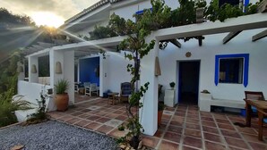 En vit byggnad med blå detaljer, en täckt uteplats med sittplatser och en grusbelagd gångväg.