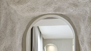 A hallway leading to a bedroom with a bed, a bedside table, and a lamp. - Mykonos Earth Suites - Adults Only (Mykonos)