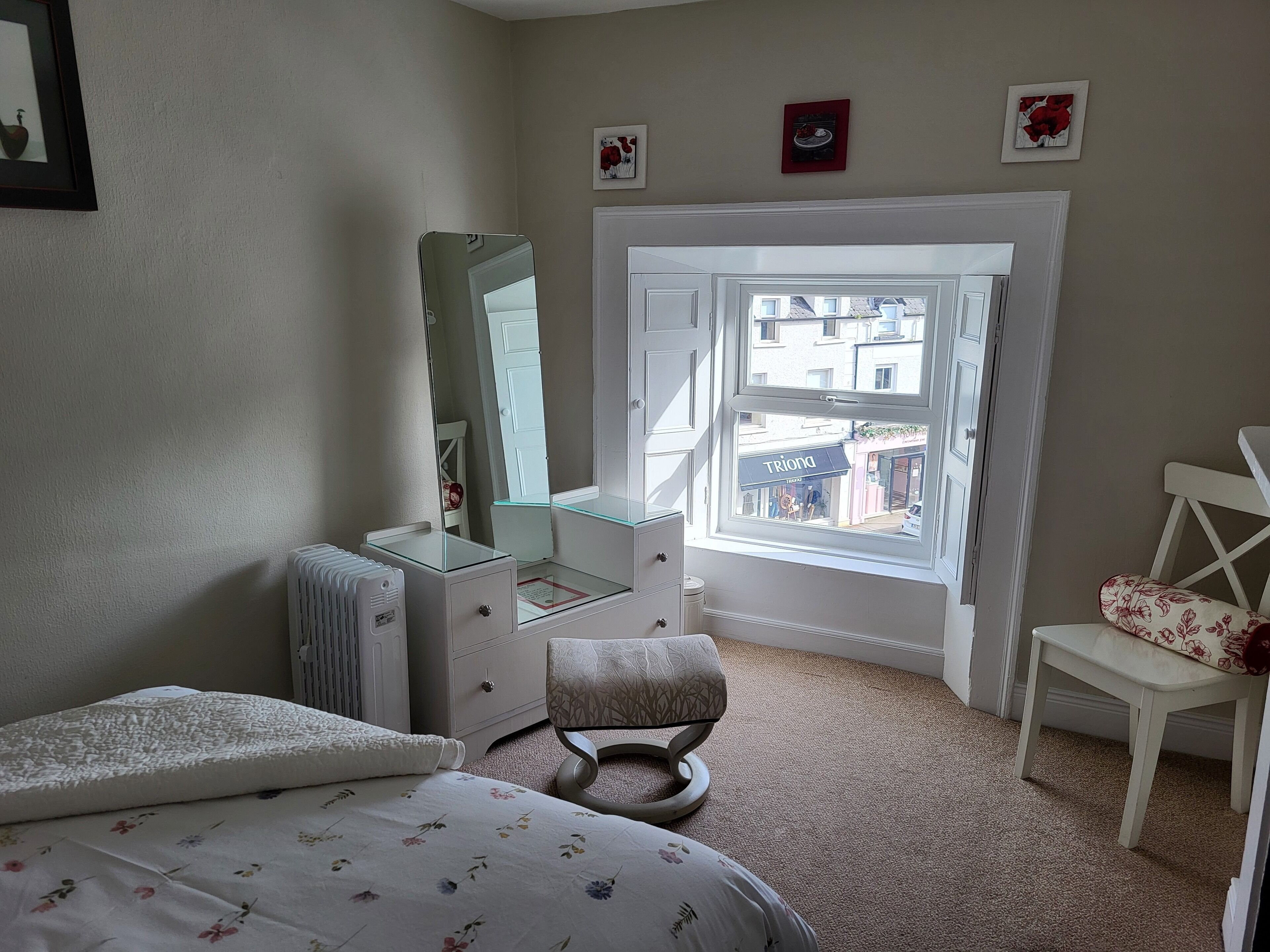 A bedroom with a bed, a dresser, a chair, a mirror, and a window with a view of the street.