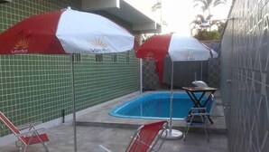 Ein Poolbereich mit zwei roten und weißen Sonnenschirmen, einem kleinen Billardtisch und zwei roten Liegestühlen.