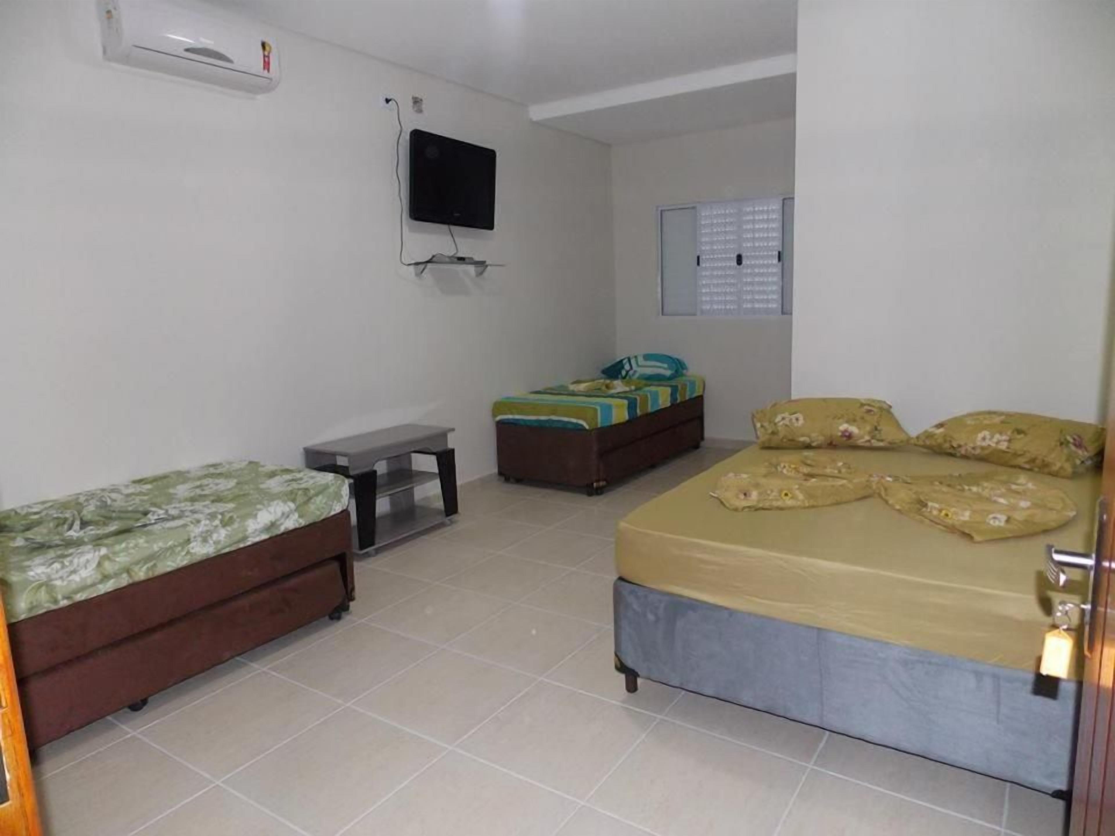 Quarto com duas camas, televisão e janela com persianas.