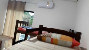Ein Schlafzimmer mit einem Bett, einem Fenster mit Vorhängen und einer Klimaanlage an der Wand.