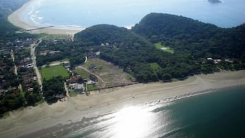 Vista aérea de uma área costeira com praia, colinas arborizadas e uma estrada.