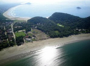 Vista aérea de una zona costera con playa, colinas boscosas y una carretera.