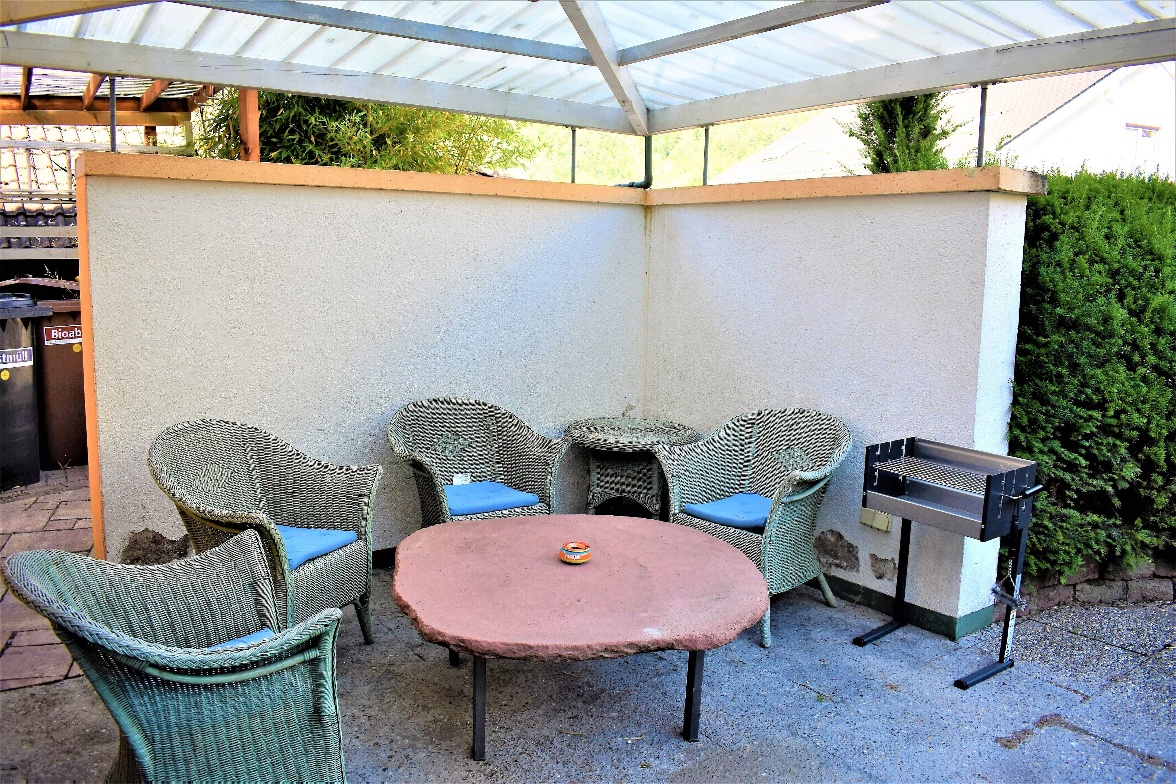 Un patio couvert aménagé avec des meubles en osier, une table ronde et un barbecue.