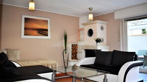 Un salon moderne avec une table basse en verre, un canapé noir et blanc, un tableau représentant un coucher de soleil encadré et une cheminée ornée d’une statue.