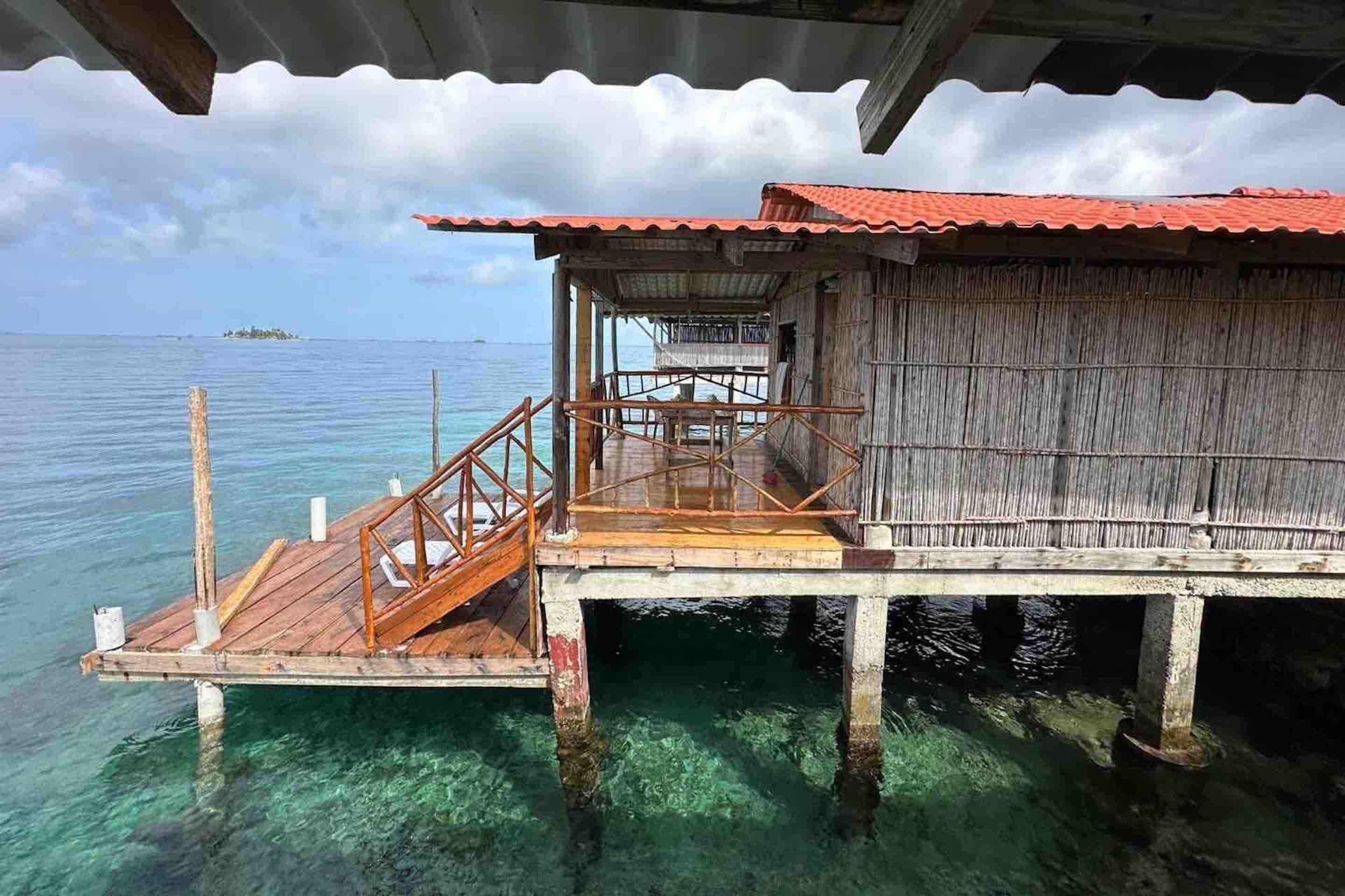 Una cabaña sobre el agua de madera con techo rojo, una terraza de madera y vistas al océano.