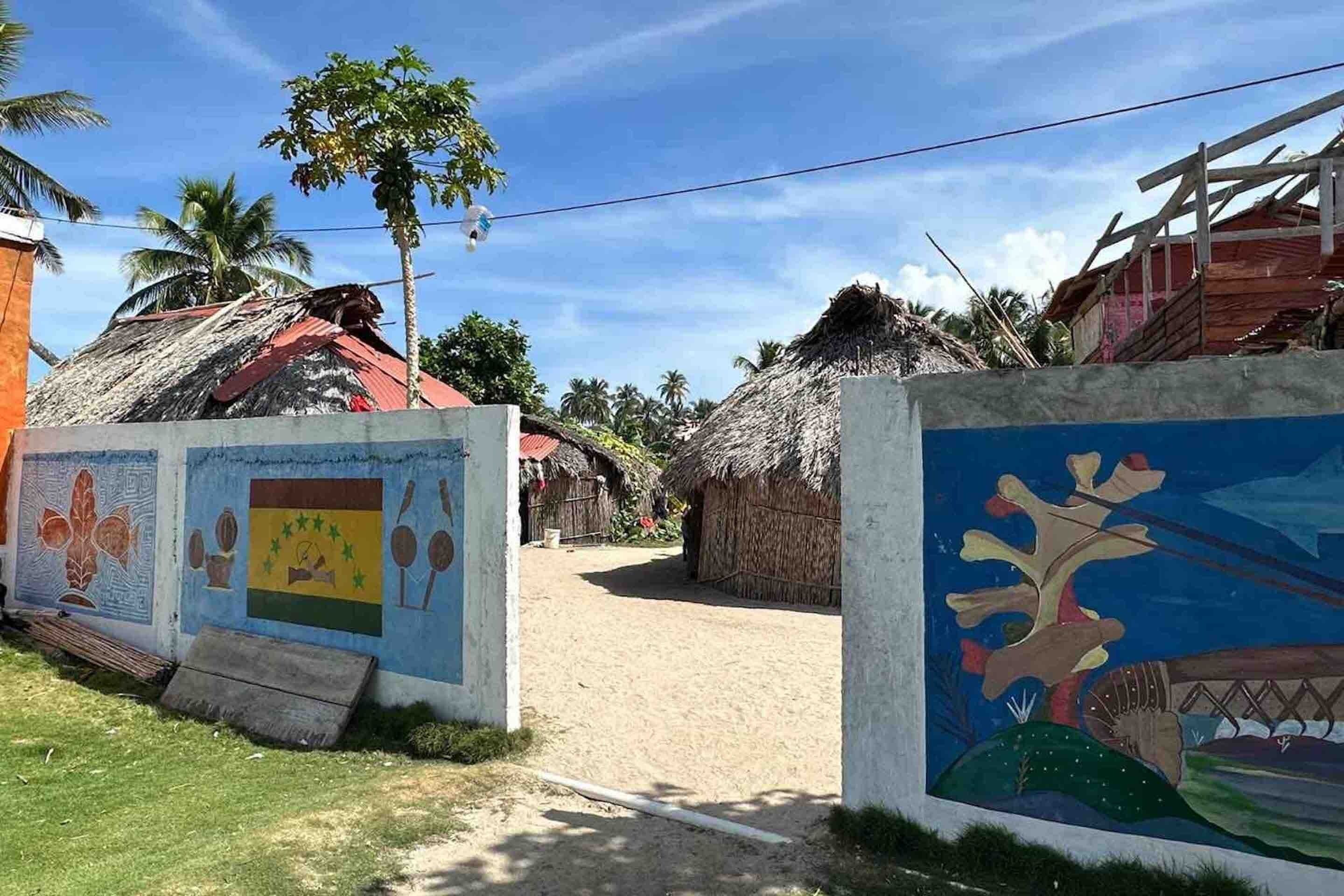 Un pueblo rural con casas de techo de paja, un camino de tierra y un mural que representa la cultura local.