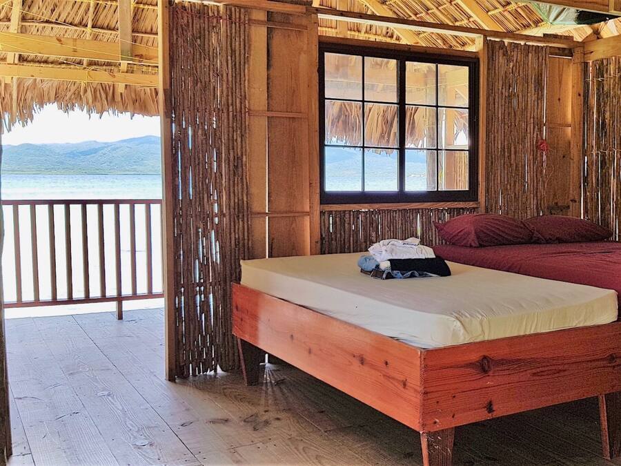 Un lit en bois avec un matelas et des oreillers, une fenêtre donnant sur la mer et un rideau en bambou.