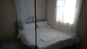 A single bed with a mosquito net, white bedding, and a tiled floor with a pattern. - Merybyplace Guest House (Kitui)