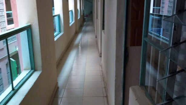 A corridor with tiled flooring, windows with metal grilles, and a view of adjacent buildings. - Merybyplace Guest House (Kitui)
