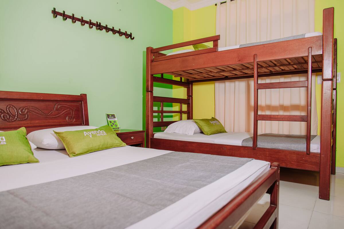 Une chambre avec des lits superposés, une tête de lit en bois et un oreiller vert orné du texte « Ayendo Hotels ».