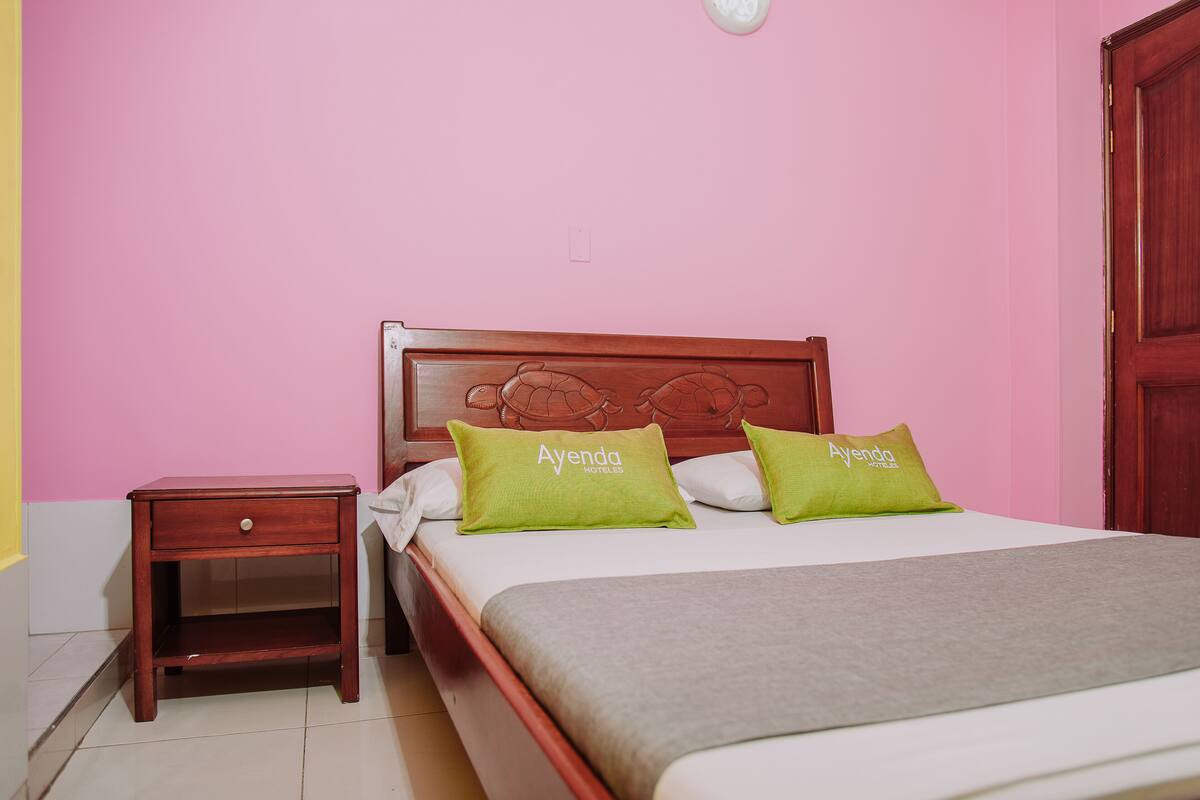 Une chambre à coucher avec une tête de lit en bois, une table de chevet, un lit avec deux oreillers verts et un mur rose.