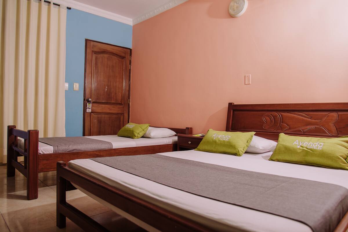 Une chambre d’hôtel avec deux lits simples, des têtes de lit en bois et des oreillers verts ornés du nom de l’hôtel.